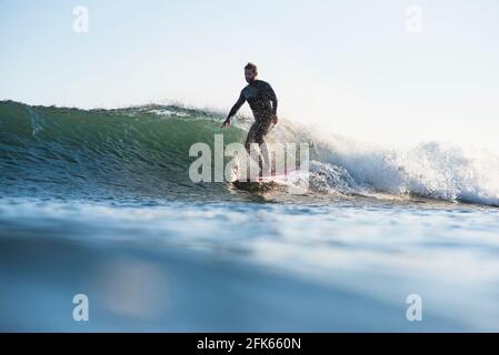 Athletic Man surfant sur une vague pendant le coucher du soleil d'été Banque D'Images