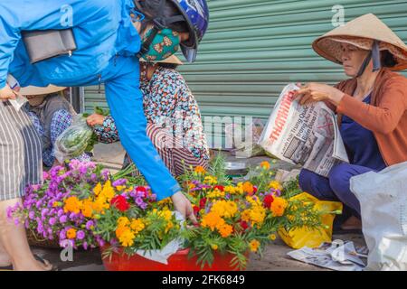 Femme vietnamienne portant un casque de moto et un masque facial choisissant des fleurs du fleuriste sur le côté de la route, Hoi an, Vietnam Banque D'Images