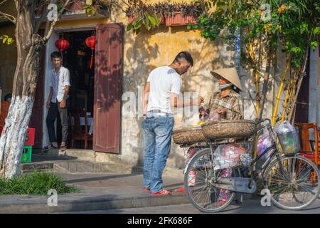 Négociant vietnamien de fruits vendant à une cliente de son vélo, Hoi an, Vietnam Banque D'Images