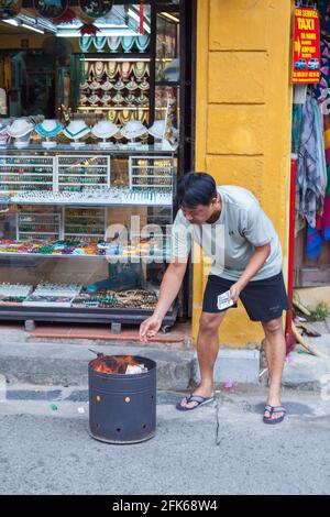 Homme vietnamien d'âge moyen brûlant de l'argent de papier votif/fantôme/esprit dans la rue, vieille ville, Hoi an, Vietnam Banque D'Images