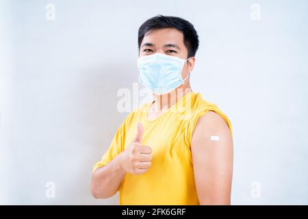 Homme asiatique portant un masque dans l'épaule avec du plâtre sur le bras après la vaccination sur fond blanc, concept de vaccination contre le coronavirus o Banque D'Images