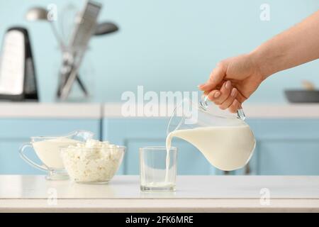 Femme versant du lait du pichet dans le verre dans la cuisine Banque D'Images