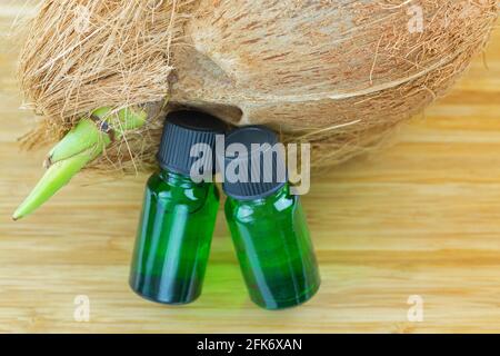 Pure Coconut essential concentrate oil extract in green bottles next to mature raw coconut shell with brown fiber and green sprout on wooden backgroun Banque D'Images