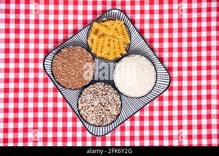 Aliments végétaux. Une assiette décorative avec quatre bols de sarrasin, nouilles, riz et quinoa sur un nappe à carreaux rouges. Une alimentation saine. Vue de dessus wi Banque D'Images