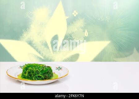 Cuisine japonaise. Salade de chuka fraîche avec sesam sur une assiette sur une table blanche devant un monde sous-marin éclairé vert abstrait. Modèle pour votre produit dis Banque D'Images