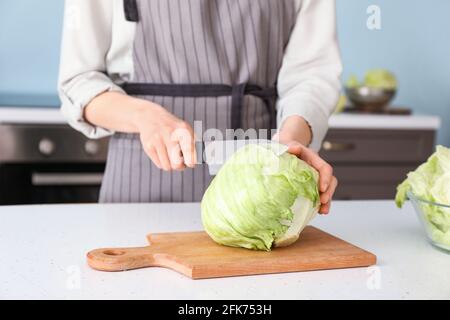 Femme coupant de la laitue iceberg sur une table dans la cuisine Banque D'Images