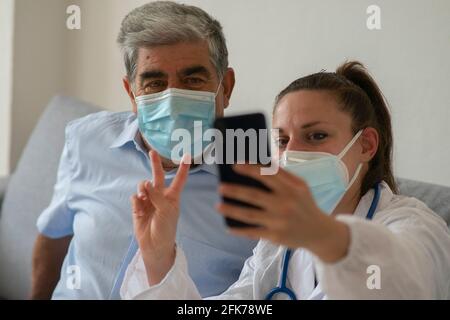 Une femme médecin avec un masque de protection célèbre le rétablissement du patient en prenant un selfie ensemble. Concept de réussite pendant les soins à domicile.Focus sur l'ap Banque D'Images