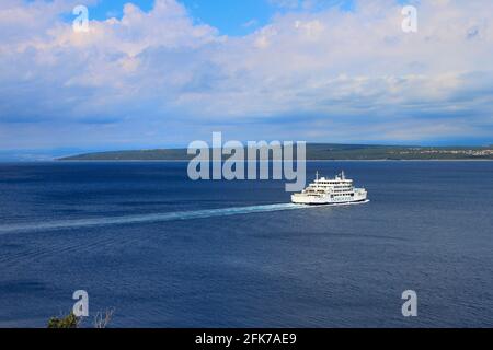 Un ferry blanc traverse une baie bleue, le ciel est bleu avec des nuages.Une île est visible au loin Banque D'Images