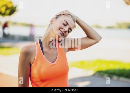 La jeune femme fait de l'exercice en plein air. Elle étire son corps et s'échauffe pour le jogging. Banque D'Images