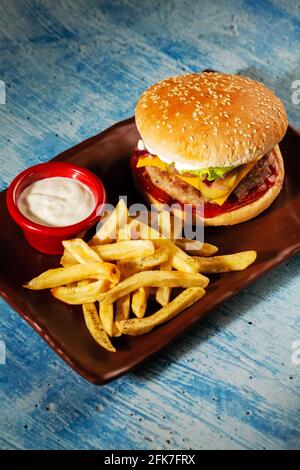 Hamburger. Côtelette de porc juteuse, cheddar, oignons croquants, laitue enveloppée dans un pain sous deux sauces. Servi avec des frites et de la sauce à la crème. Banque D'Images