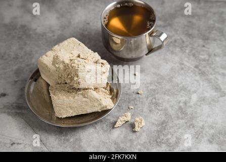 Une assiette métallique avec halva de tournesol et une tasse de thé vert sur la table. Banque D'Images