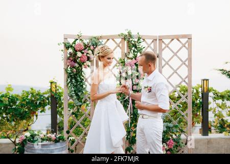 La mariée et le stand de marié près de l'arc de mariage, le marié met l'anneau sur le doigt de la mariée pendant la cérémonie de mariage Banque D'Images