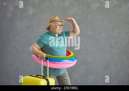 Drôle homme âgé dans un cercle gonflable et avec une valise regarde en arrière-plan. Banque D'Images