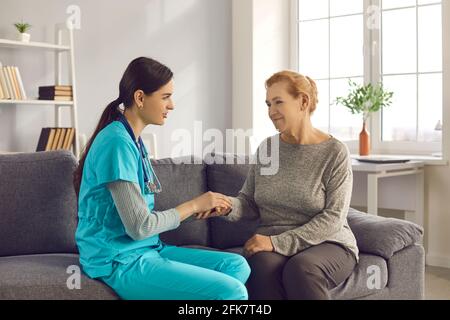 Une infirmière soutient une patiente âgée qui tient la main lors d'une visite médicale à domicile. Banque D'Images