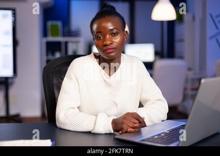 Femme d'affaires fatiguée et concentrée regardant l'appareil photo après avoir lu des tâches sur le site d'un ordinateur portable au bureau de la start-up entreprise tard dans la nuit. Employé faisant des heures supplémentaires pour un emploi dans le respect de la date limite Banque D'Images