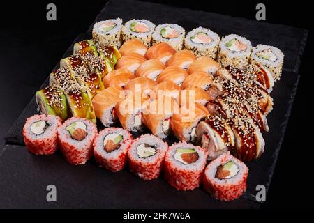 Sushi ensemble de différents rouleaux avec différentes garnitures sur une ardoise de pierre noire. Concept de délicieuse cuisine traditionnelle japonaise, délicieux fruits de mer a Banque D'Images