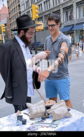 Dans le cadre de la sensibilisation de Chabad Lubavitch, un jeune étudiant juif aide un autre juif à faire le bon acte de porter des phylacaractéristiques. À Union Square Park, New York. Banque D'Images