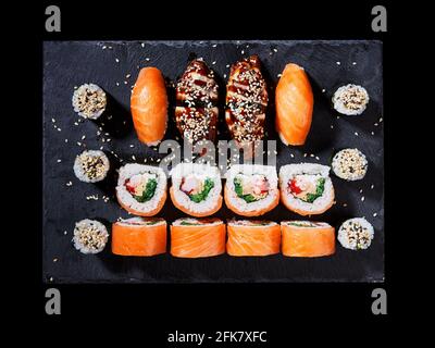 Vue de dessus de délicieux sushi avec des petits pains de Californie, sashimi et maki sur une assiette noire. Cuisine orientale japonaise avec poisson cru, fromage, graines de sésame Banque D'Images