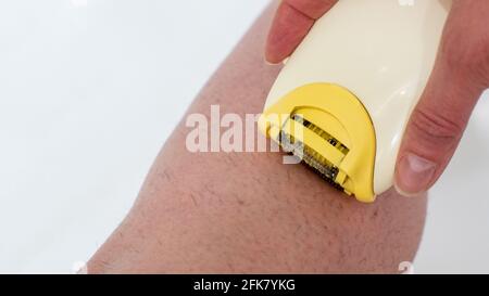 Un gros plan d'une main féminine élimine l'excès de poils des jambes à l'aide d'un rasoir électrique. Soins de beauté à la maison. Hygiène de la peau concept de soins du corps. Dépilatio Banque D'Images