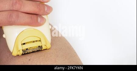 Un gros plan d'une main féminine élimine l'excès de poils des jambes à l'aide d'un rasoir électrique. Soins de beauté à la maison. Hygiène de la peau concept de soins du corps. Dépilatio Banque D'Images