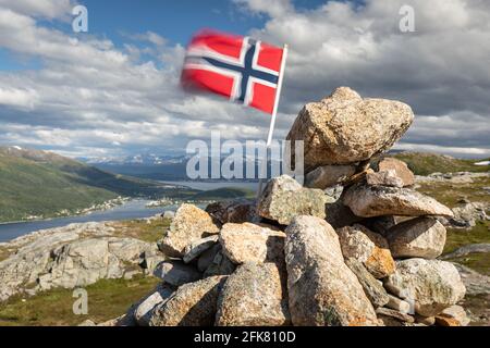 Drapeau norvégien dans le vent au sommet des montagnes. Rochers, fjord, ville de Tromso et montagnes enneigées en arrière-plan Banque D'Images