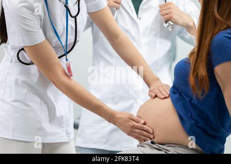 Une femme médecin vérifie l'abdomen d'une femme enceinte en touchant ses mains. Bureau médical professionnel. Vue rapprochée. Banque D'Images