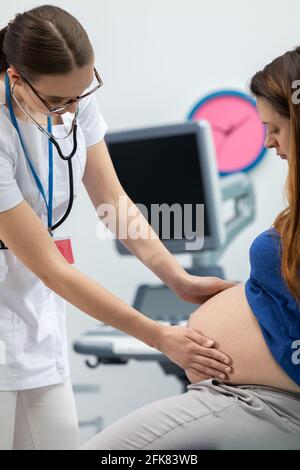 Un médecin vérifie l'abdomen d'une femme enceinte en le touchant avec ses mains. Un bureau de médecin professionnel Banque D'Images