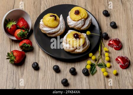 Composition d'un plat avec dessert italien typique appelé zeppole, fraises, bleuets, chocolats en forme de coeur et fleurs mimosa Banque D'Images