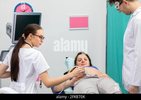 Une infirmière effectue une échographie sur un patient enceinte sous la direction du médecin traitant. Banque D'Images