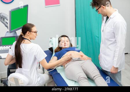 Une infirmière effectue une échographie sur un patient enceinte sous la direction du médecin traitant. Écran vert. Banque D'Images