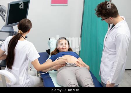 Une infirmière effectue une échographie sur un patient enceinte sous la direction du médecin traitant. Banque D'Images