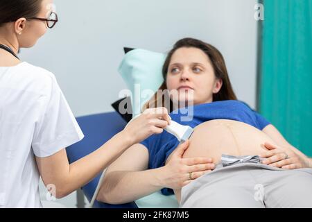 Dans la salle de gynécologie, une femme médecin examine une femme enceinte à l'aide d'un échographe. Banque D'Images