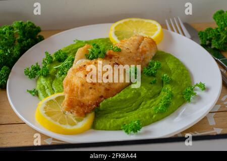 repas maison avec poisson frit et purée de pois verts servi avec une tranche de citron sur une assiette blanche avec un couteau et la fourchette Banque D'Images