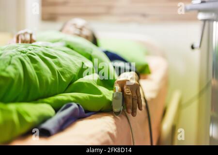 Femme âgée couchée sur un lit portant un oxymètre de pouls du bout des doigts dans le bloc opératoire. Banque D'Images