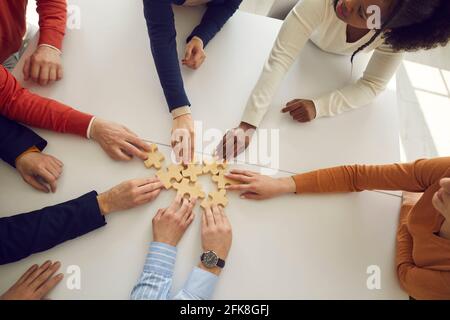 Les employés de bureau multiraciaux assemblent des puzzles en bois sur le bureau symbolisant le développement et le succès. Banque D'Images