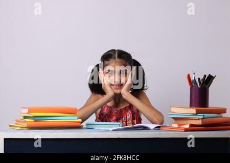 petite fille indienne pensant ou rêvant pendant la préparation des devoirs. avec pile de livres Banque D'Images