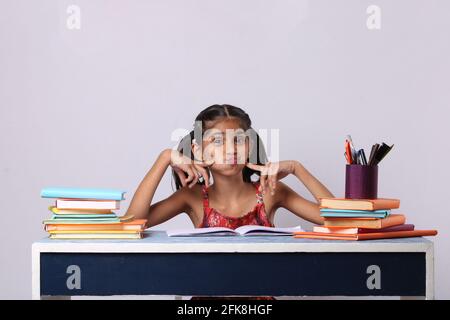 petite fille indienne pensant ou rêvant pendant la préparation des devoirs. avec pile de livres Banque D'Images