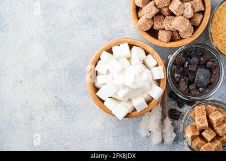 Sucre blanc, cubes de sucre de canne, caramel dans un bol en bambou sur fond de béton de table gris. Différents types de sucre assortis. Vue de dessus ou plan de travail. Banque D'Images