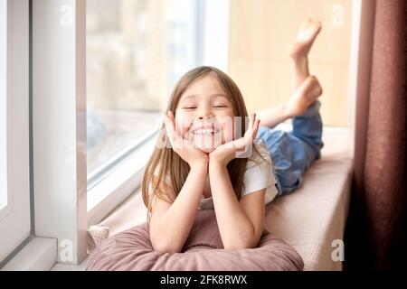 Bonne journée pour les enfants. Journée de la protection des enfants. Une fille souriante et gaie se trouve sur le rebord de la fenêtre en vacances Banque D'Images