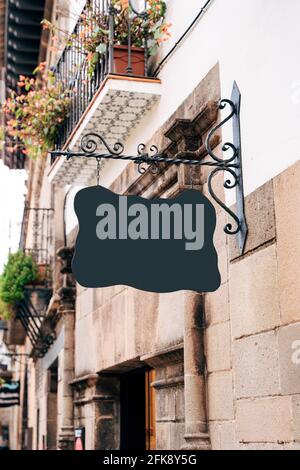 Un panneau vide de forme bizarre est suspendu sur un beau broche forgée sur la façade d'un ancien bâtiment contre la toile de fond des balcons avec pots de fleurs Banque D'Images