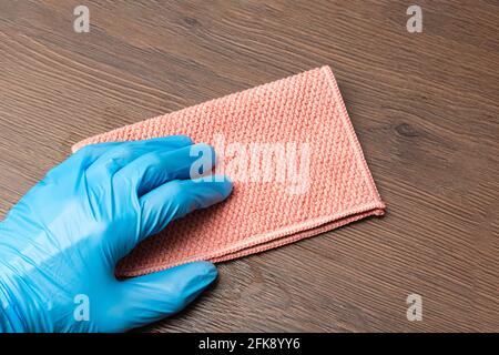 Nettoyage de la maison. Les mains dans les gants en latex essuyent une surface en bois avec un chiffon en microfibre rose, gros plan. La femme de ménage époussait les meubles dans le Banque D'Images