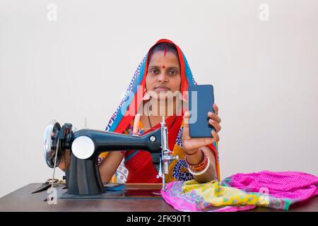 Femme rurale indienne utilisant la machine à coudre et MONTRANT SON MOBILE TÉLÉPHONE Banque D'Images