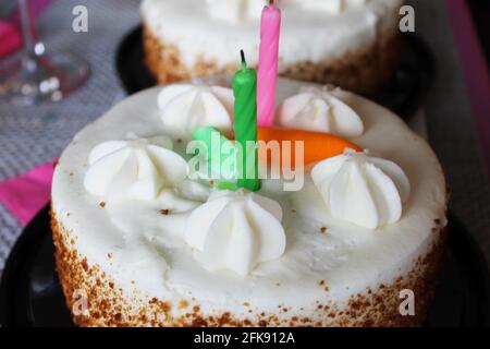 Gros plan d'un gâteau d'anniversaire à la carotte, avec deux bougies, et une carotte orange givrante sur le dessus. Banque D'Images