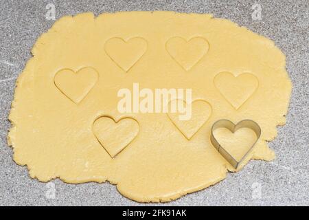 Biscuits coupés au coeur et forme de coeur pour couper sur la pâte jaune crue sur un fond de table gris. Étalez la pâte et découpez les biscuits en forme de coeur pour cuire Banque D'Images