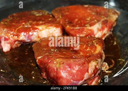 Gros plan de steaks crus marinant sur une plaque de verre transparent. Banque D'Images