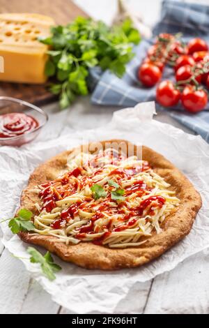 Délicieux langos frits servis sur du papier de cuisson avec beaucoup de fromage râpé, ketchup et herbes fraîches. Banque D'Images