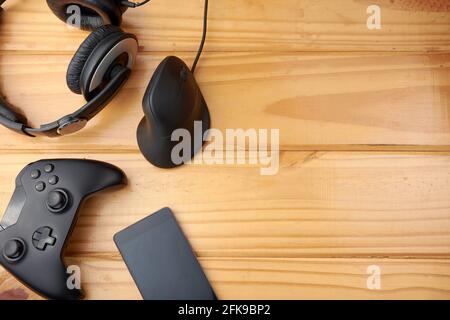 Vue de dessus des accessoires de jeu ergonomiques avec manette de jeu, souris verticale, casque et téléphone portable sur une table rustique en bois. Banque D'Images