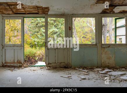 Intérieur de la maison abandonnée. Galerie avec cadres de porte et de fenêtre, verre brisé et plâtre tombé, jardin d'automne surcultivé vu par les fenêtres Banque D'Images