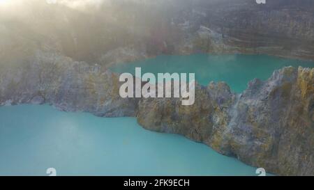 Vol au-dessus des lacs de Vulanice à basse altitude. Vue rapprochée d'un mur de roche séparant les lacs colorés. Cratère volcanique de trois couleurs Kelimutu couvert Banque D'Images