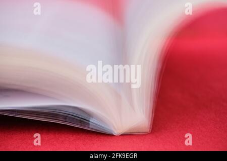 Sur fond rouge luxuriant, cette image à longue exposition capture les pages blanches d'un livre en mouvement lorsqu'elles sont retournées. Banque D'Images